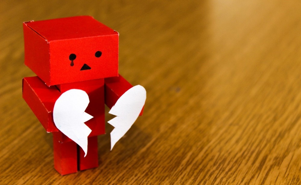 red paper block robot holding two halves broken heart